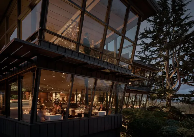 Canlis at dusk: the midcentury glass-walled dining room lit from within, seen from outside through evergreens.