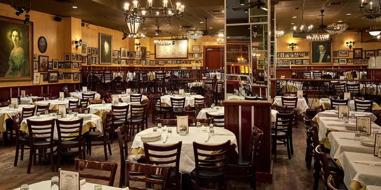 Carmine's Times Square dining room: round banquet tables under chandeliers in a high-ceilinged room hung with framed pictures.